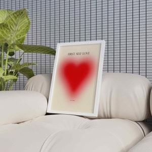 May include: A white framed print with the text "FIRST, SELF LOVE" and a red heart graphic. The print is sitting on a white couch.