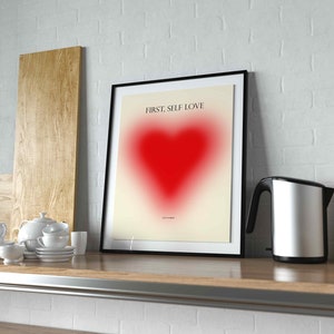 May include: A framed print with a black frame and a white background. The print features a red heart with a gradient effect and the text "FIRST, SELF LOVE".