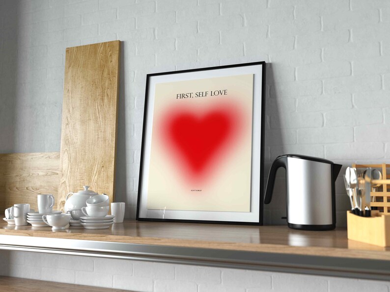 May include: A framed print with a black frame and a white background. The print features a red heart with a gradient effect and the text "FIRST, SELF LOVE".