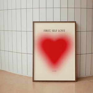 May include: A framed print with a red heart shape and the text "FIRST, SELF LOVE" in black.