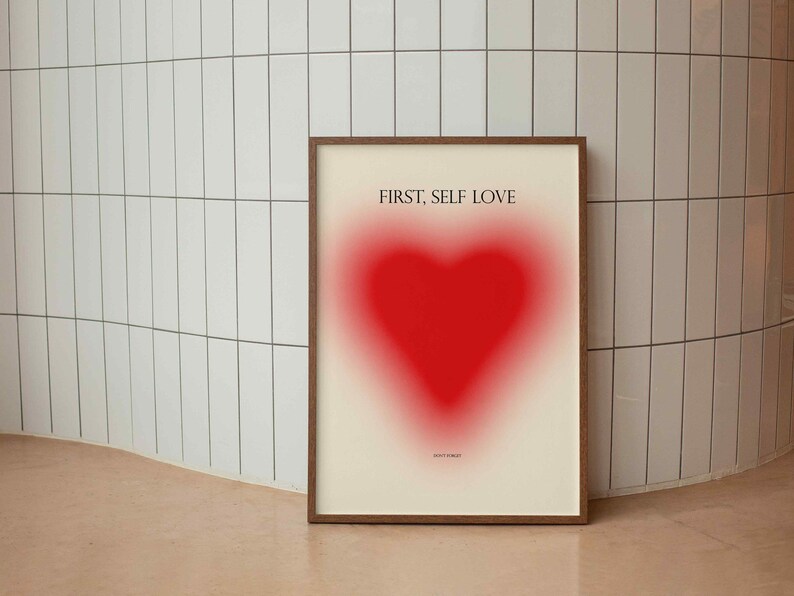 May include: A framed print with a red heart shape and the text "FIRST, SELF LOVE" in black.