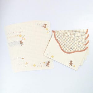 May include: Set of stationery featuring a grid pattern and illustrations of bears. The paper is cream colored with a light brown grid pattern. The envelopes are cream colored with a brown grid pattern and a scalloped edge.