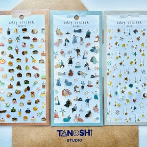 May include: Three sheets of stickers with different themes. The first sheet features a variety of sweets, including cakes, cookies, and pastries. The second sheet features people in various poses, including sitting, standing, and walking. The third sheet features stars and other celestial objects. Each sheet has the text "Cozy Sticker" and a sub-theme.