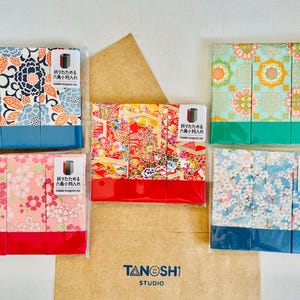 May include: An assortment of hexagonal cases with colorful floral and geometric patterns. Each case is packaged in clear plastic and features a label with Japanese text. The cases are displayed on a light brown surface.