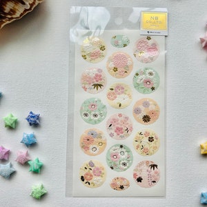 May include: A sheet of 16 round stickers with floral designs. The stickers are in shades of pink, green, and yellow. The stickers are on a white background. The text "NB CO.,LTD. JAPAN" is printed on a white label in the top right corner.