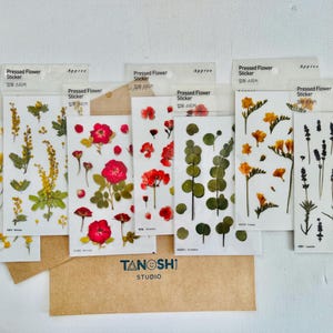 May include: Eight sheets of pressed flower stickers with various flower designs. The stickers feature pressed flowers in shades of yellow, red, purple, and green. The stickers are labeled "Pressed Flower Sticker" and "Appree".