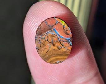 May include: A round, brown opal cabochon with blue and green iridescence. The opal is set in a clear resin.