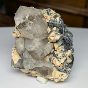May include: A natural quartz crystal cluster with a clear, crystalline structure. The quartz is set against a matrix of beige and dark blue minerals, creating a striking contrast. The specimen is a unique geological formation.