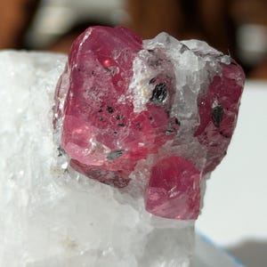 May include: A vibrant pink ruby crystal with a rough, natural texture. The crystal is embedded in a white, crystalline matrix.