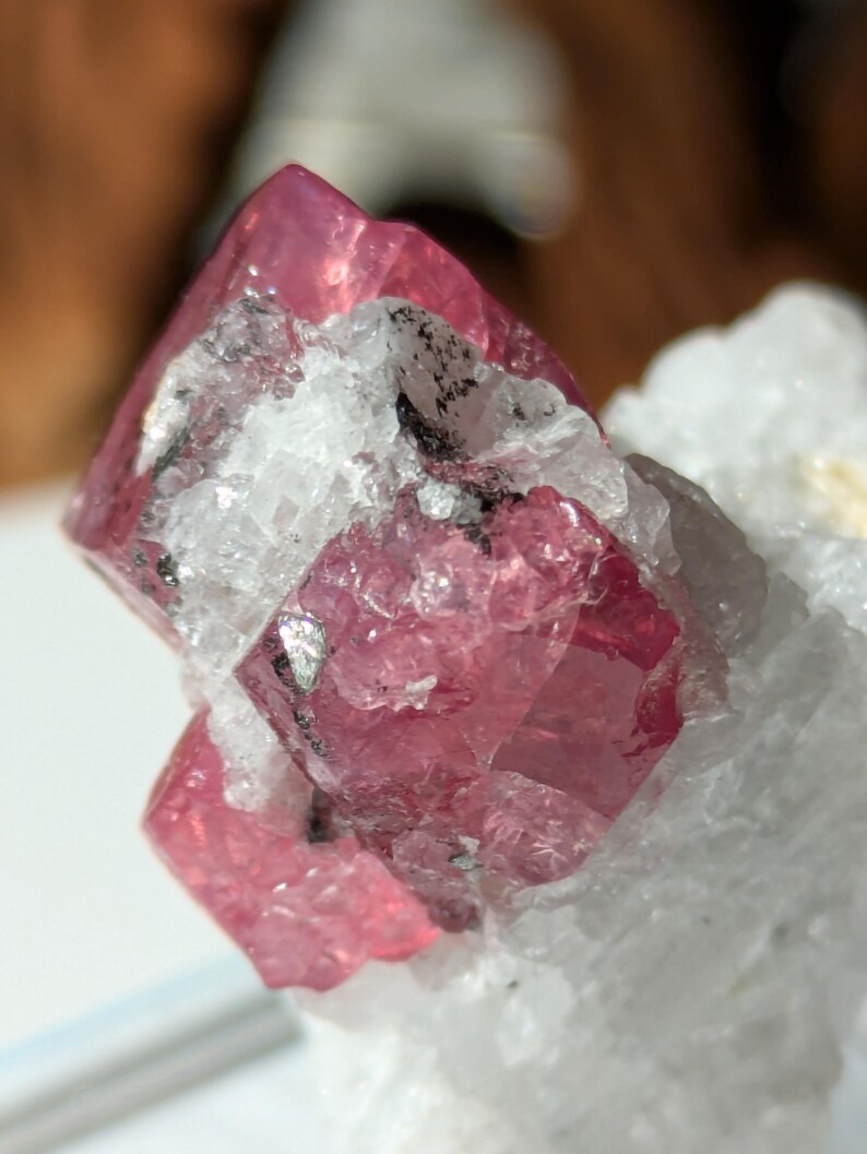May include: A cluster of pink crystals with a glassy, translucent appearance. The crystals are embedded in a white, opaque matrix.