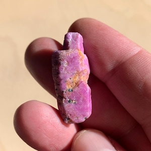 May include: A pink ruby crystal with black inclusions. The crystal is rough and has a natural, unpolished appearance.