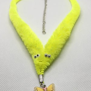 May include: A bright yellow fuzzy necklace with a butterfly charm. The necklace is shaped like a worm with two googly eyes.