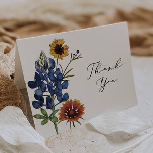 May include: A white card with a floral design and the text "Thank You". The flowers are blue, yellow, and red.