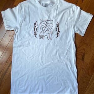 May include: White t-shirt with a crew neck and short sleeves. The shirt features a brown graphic of a winged creature with the text "I'M AN ANIMAL TOO" above the creature.
