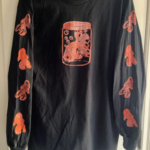 May include: Black long-sleeve t-shirt with an orange goldfish in a jar graphic on the front and orange goldfish graphics on the sleeves.