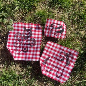 May include: Three red and white gingham fabric squares with black ink drawings of a butterfly, a ladybug, and a unicorn.