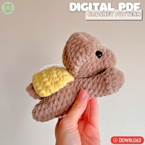 May include: A crocheted turtle toy in brown and yellow. The turtle has a soft, textured appearance, with a yellow shell and black eyes. The image includes the text "DIGITAL PDF CROCHET PATTERN" and a download button.