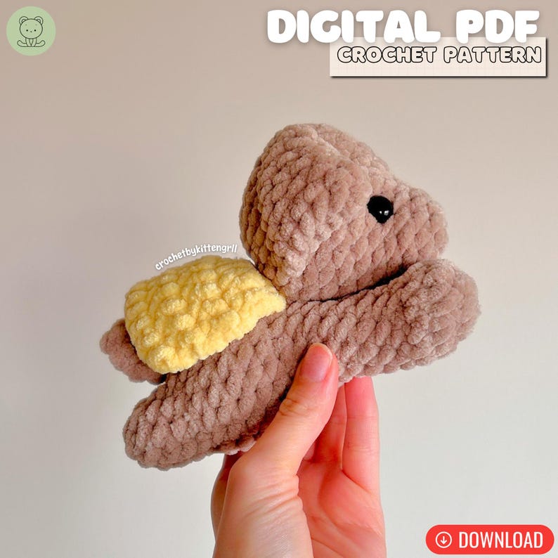 May include: A crocheted turtle toy in brown and yellow. The turtle has a soft, textured appearance, with a yellow shell and black eyes. The image includes the text "DIGITAL PDF CROCHET PATTERN" and a download button.