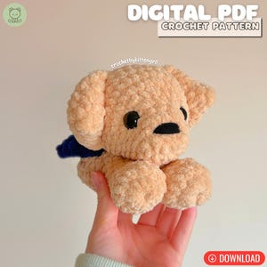 May include: A crocheted plush puppy in a light tan colour with black eyes and nose, and a dark blue scarf. The image includes the text "DIGITAL PDF CROCHET PATTERN" and the Etsy shop name "crochetbykittengrll".