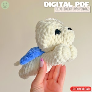 May include: A white crocheted toy with black eyes and a blue wing. The image includes the text "DIGITAL PDF CROCHET PATTERN" and the word "DOWNLOAD" in a red circle.