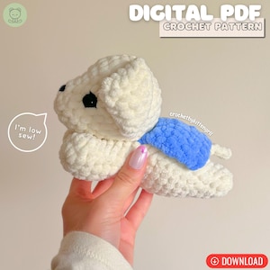 May include: A cream-coloured crocheted dog with a blue accent. The dog has black eyes and is lying down. Text at the top reads "DIGITAL PDF CROCHET PATTERN". A speech bubble says "I'm low sew!"