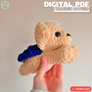 May include: A beige crocheted teddy bear with a blue accent on its back. The bear has black eyes and is held in a hand. Text on the image reads "DIGITAL PDF CROCHET PATTERN" and "crochetbykittengrrl". A download button is visible.