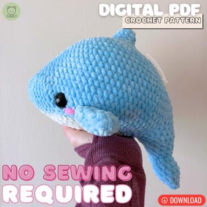 Könnte beinhalten: Ein hellblaues gehäkeltes Wal-Kuscheltier mit weißem Bauch, schwarzen Sicherheitsaugen und kleinen rosa Wangen. Der Text DIGITAL PDF CROCHET PATTERN und NO SEWING REQUIRED ist sichtbar. Das Kuscheltier hat eine weiche, strukturierte Garnoberfläche.