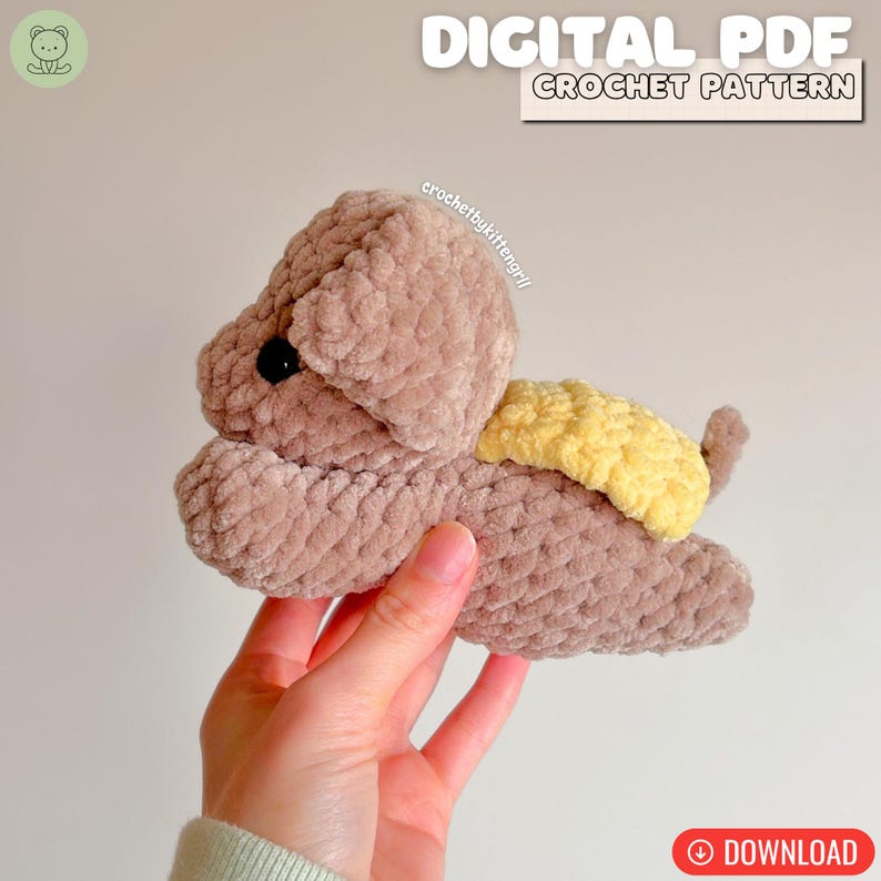 May include: A crocheted plush puppy in shades of brown and yellow. The puppy has a textured, soft appearance, with a yellow wing-like detail on its back. The image includes the text "DIGITAL PDF CROCHET PATTERN" and a download button.