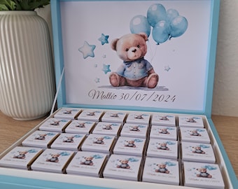 May include: A light blue box with a lid, filled with small white boxes. The lid has a picture of a teddy bear with blue balloons and stars. The text "Matteo 30/07/2024" is printed on the lid.