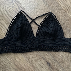 May include: A black crochet top with a triangle-shaped bodice and crisscross straps. The top features a detailed crochet stitch pattern and ties at the back. This handmade top is perfect for summer wear.