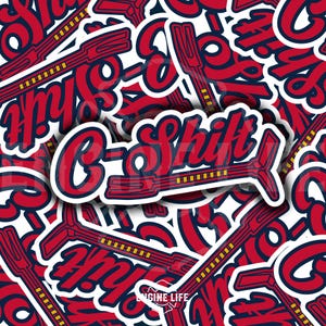 May include: Red and blue sticker with the text "C-Shift" and a stylized gear design. The sticker has a white border and a yellow and black striped pattern on the gear.