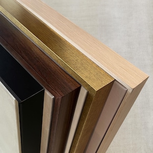 May include: A selection of wooden picture frames in various colors, including black, dark brown, gold, and light wood tones. The frames are angled, showcasing their different finishes and textures. The image highlights the variety of frame styles available.