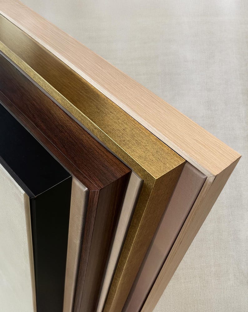 May include: A selection of wooden picture frames in various colors, including black, dark brown, gold, and light wood tones. The frames are angled, showcasing their different finishes and textures. The image highlights the variety of frame styles available.