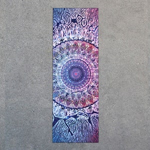 May include: A long, rectangular yoga mat with a colorful mandala design. The mandala features a central circle with intricate patterns in shades of pink, purple, and blue. The background of the mat is a dark blue with white and black details.