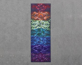 Puede incluir: Una colorida esterilla de yoga con un diseño de arcoíris que presenta intrincados patrones y símbolos. La esterilla está dividida en siete secciones, cada una representando un chakra diferente.