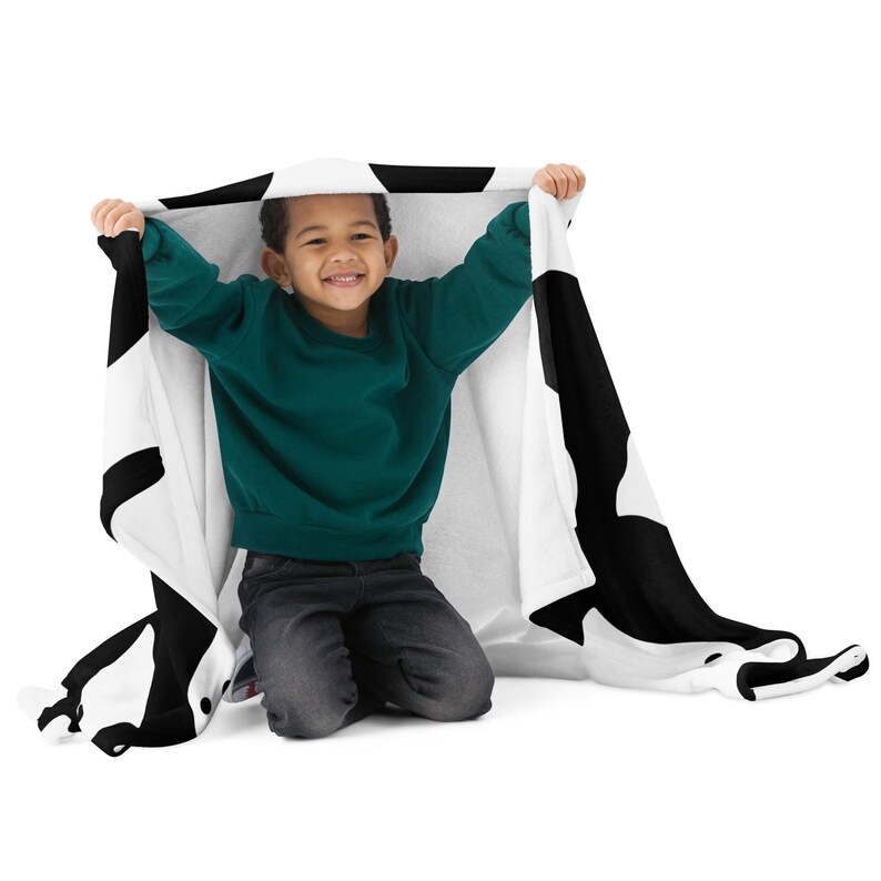 May include: A child is sitting on the floor, playing with a black and white patterned blanket. The blanket has a large black and white design on it.