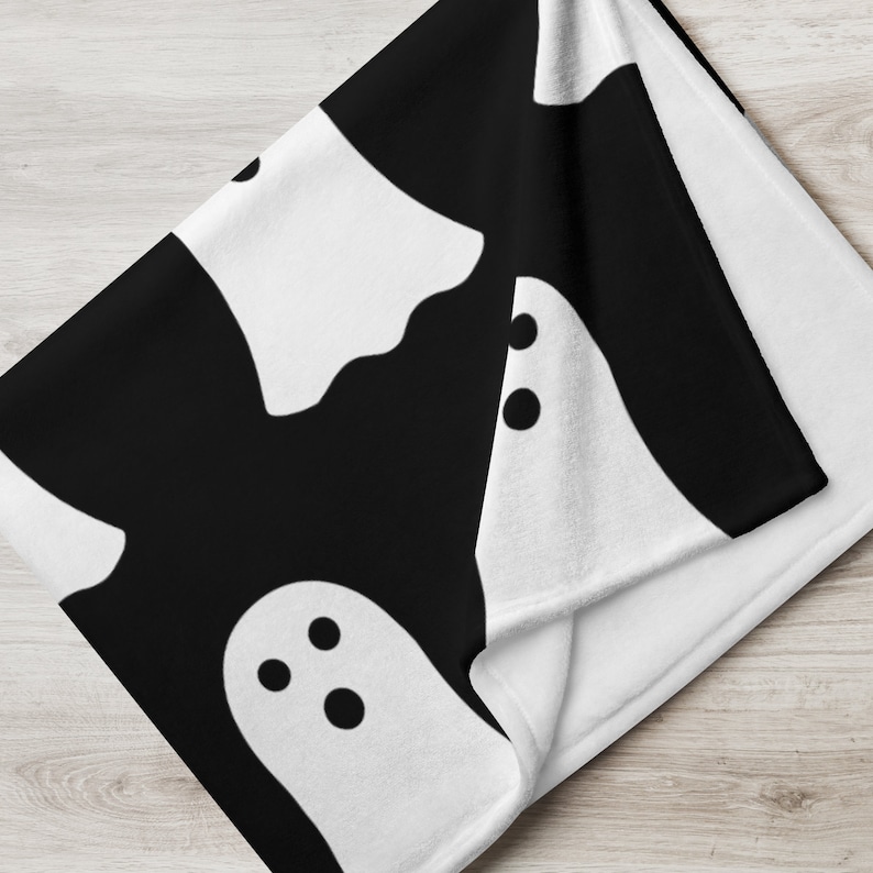 May include: Black and white throw blanket with a repeating pattern of white ghosts with black eyes.