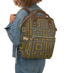 May include: A brown leather backpack with a geometric pattern in shades of yellow, green, and pink. The backpack has a large main compartment and a smaller front pocket.