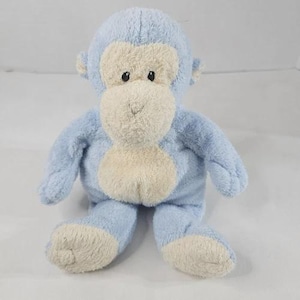 May include: A plush monkey toy featuring soft light blue fur with a cream-colored face, belly, and feet. The stuffed animal has embroidered black eyes and a stitched nose and mouth, with a rounded head and long arms and legs in a seated position.