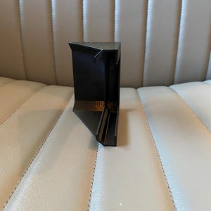 May include: A black, geometric, angular object with a triangular top and a rectangular base. The object has a modern design and appears to be made of a solid, dark material. The object is positioned on a light-coloured surface.