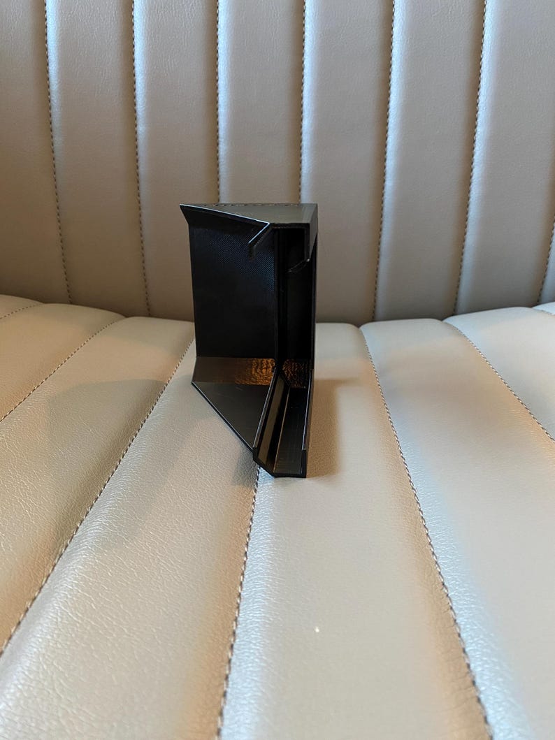 May include: A black, geometric, angular object with a triangular top and a rectangular base. The object has a modern design and appears to be made of a solid, dark material. The object is positioned on a light-coloured surface.