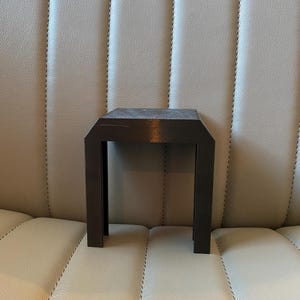 May include: A small, dark brown wooden side table with a square top and four straight legs. The table is made of a dark wood and has a simple, modern design. The table is approximately 30 cm tall.