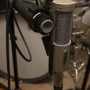 May include: Two professional microphones are shown. One is a black Shure microphone, and the other is a silver and black R-10 microphone. The image also includes a "Proudly Made in USA" sticker.