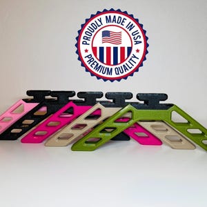 May include: A collection of colorful, angled stands in pink, black, tan, green, and pink. Each stand has a black top and a series of rectangular cutouts. The image includes a "Proudly Made in USA" emblem.