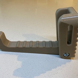 May include: A tan-colored, 3D-printed step stool with a textured surface. The stool has a curved footrest and a notched edge for stability. A screw secures the vertical support.