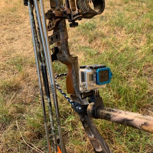 May include: A camouflage-patterned compound bow with three arrows attached to the side. A GoPro camera is mounted on the bow.