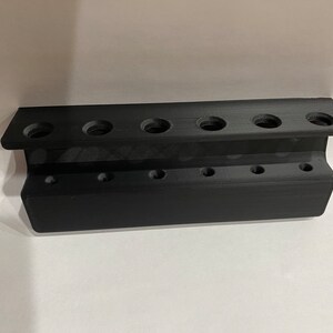 Może przedstawiać: Czarny plastikowy organizer na narzędzia z 10 otworami do przechowywania narzędzi. Organizer ma dwa rzędy otwor&oacute;w, po pięć otwor&oacute;w w każdym rzędzie.
