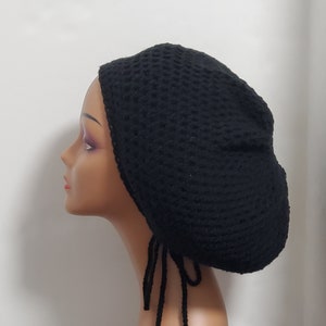 May include: Black crochet beanie with long ties and colorful beads. The beanie is made with a loose knit stitch and has a rounded shape.