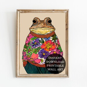 Puede incluir: Una ilustración digital de una rana marrón que lleva un suéter floral colorido. La rana está mirando directamente al espectador. El fondo es de color beige claro. El texto "INSTANT DOWNLOAD PRINTABLE WALL ART" está en un círculo en la parte inferior de la imagen.