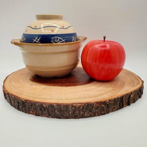 Puede incluir: Una olla de cerámica con un diseño azul y blanco se encuentra sobre una bandeja de servir de madera con una manzana roja.